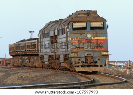 Front view of a locomotive with wagons hitched, illuminated by the setting sun. Railway track goes left. Horizontal shot.