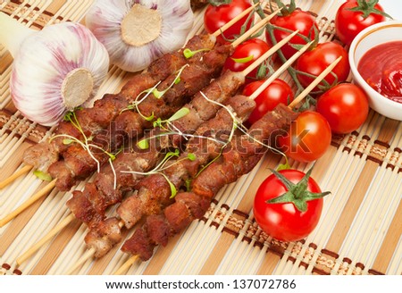 Pork skewers with cherry tomatoes, garlic and herbs. On a bamboo mat.