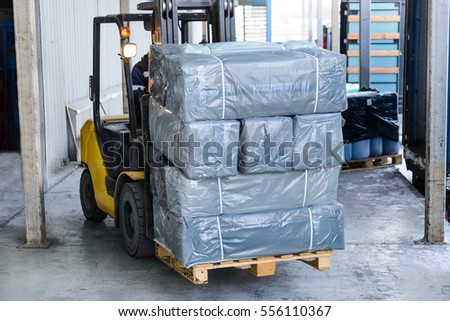 Electric forklift carries boxes. Cargo packed in polyethylene film gray.
