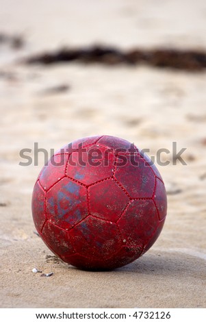 An old soccer ball/football on sand at the beach. Portrait orientation.