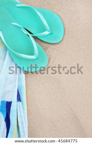 A pair of flip flops and beach towel on the sand.