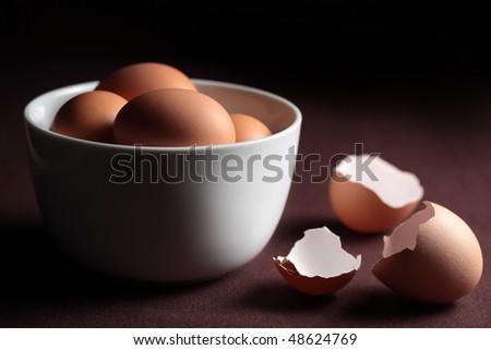 A bowl of fresh eggs and cracked egg shells on a dark background.