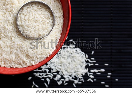 Raw white rice in a red bowl on a dark background.