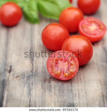 Fresh, ripe cherry tomatoes on an old chopping board. Basil leaves in the background.