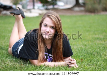Beautiful young woman posing in park, laying on stomach and feet crossed in back