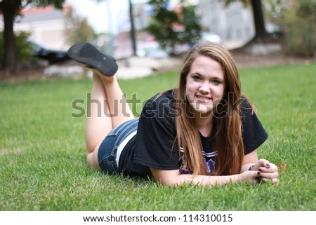 Young woman posing in park, laying on stomach and feet crossed in back