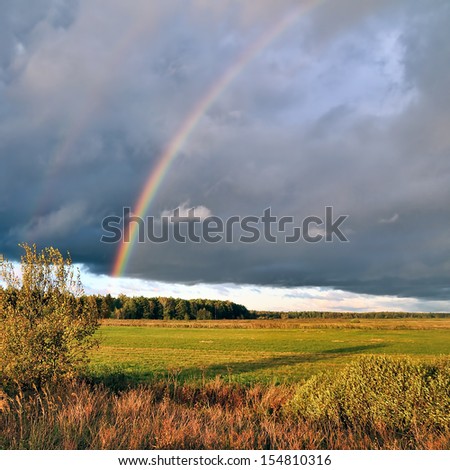 Natural double rainbow over autumn field and dark sky. After thunderstorm