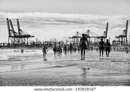 VALENCIA, SPAIN - OCTOBER 5, 2013: Crowded urban beach in the morning with the port at the background. People a jogging and swimming at the El Cabanyal Beach (Las Arenas)