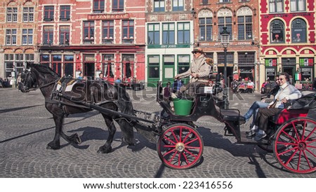 BRUGES, BELGIUM - MARCH 8, 2014: Tourists riding a Horse carriage in front of famous old colorful buildings at Market square. Popular Flemish city with almost intact medieval architecture.