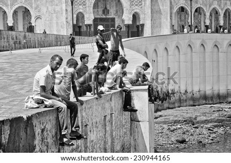 CASABLANCA, MOROCCO - AUGUST 18, 2011: Local people sitting at the pavement in front of King Hassan II Mosque. It is the largest Mosque in the country