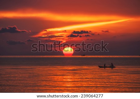 Sunset over the sea at amazing Ko Phangan in Thailand with a single boat and sun sinking below the horizon line