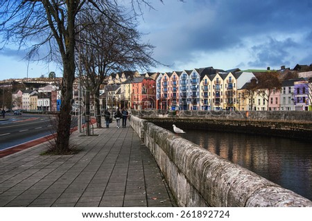 CORK, IRELAND - DECEMBER 7, 2014: Bank of the river Lee in city center with various shops, bars and restaurants. People walking at the street of third largest city in country