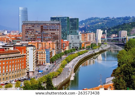 Aerial view of Bilbao, Spain city downtown with a Nevion River, Zubizuri Bridge and promenade. Mountain at the background, clear blue sky.