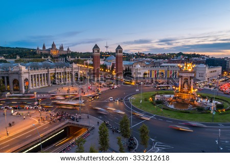 Spanish Square aerial view in Barcelona, Spain at night. This is the famous place with traffic light trails, fountain and Venetian towers, and National museum at the background. Blue sky