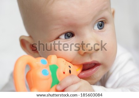 Portrait of a cute 6 month old baby, boy or girl, playing with a teething toy.