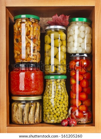 many glass bottles with preserved food in wooden cabinet