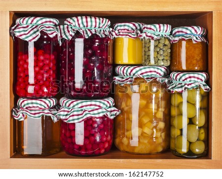 many glass bottles with preserved set food in wooden cabinet