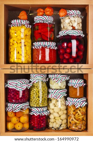Collection of many glass bottles with preserved food in wooden cabinet
