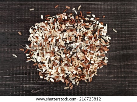 colorful blend of several varieties whole grain rice in a rustic wooden surface background