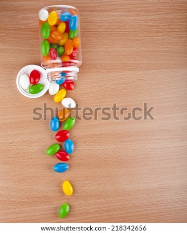 Colored  JellyBeans Pills spilled from a bottle  on surface wooden table. top view