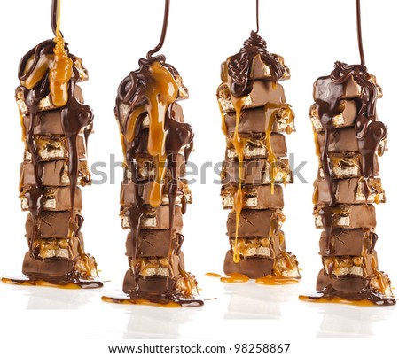 Chocolate and caramel syrup poured on stack tower of chocolate pieces on white background