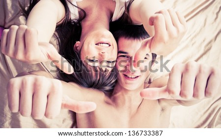 Happy couple lying on bed with thumbs up
