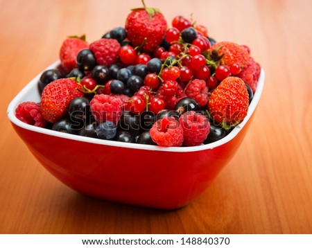 Blueberry, strawberry, raspberry, black and red currant in red bowl on table