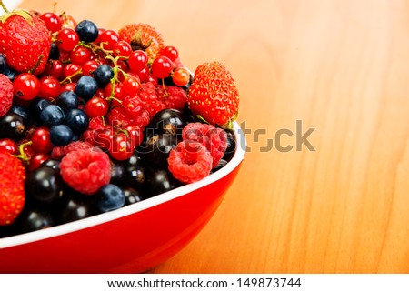 Blueberry, strawberry, raspberry, black and red currant in red bowl on table