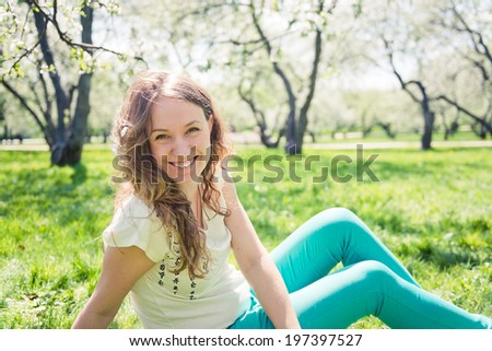 Beautiful laughing girl in green jeans sits on green grass.