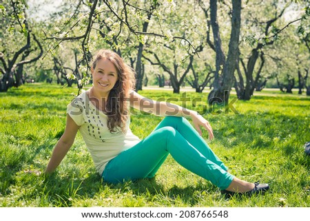 Beautiful laughing girl in green jeans sits on green grass.