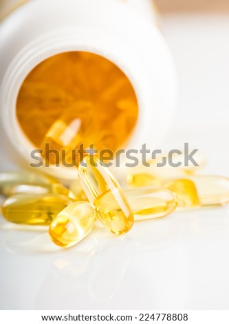 shiny yellow vitamin e fish oil capsule  spilling out of pill bottle