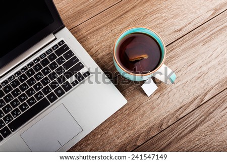 Office workplace with open laptop and cup of tea on wooden desk