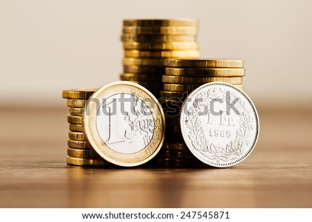 one euro coin and one swiss frank and gold money on the desk