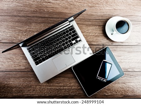 Office workplace with open laptop, tablet pc, phone and cup of coffee on wooden desk