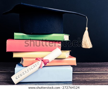 A mortarboard and graduation scroll, tied with red ribbon, on a stack of books
