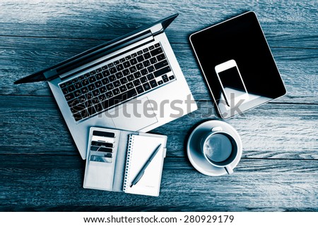 Office desk with laptop computer, tablet pc, planner, pen, mobile smartphone and cup of tea. Blue toned