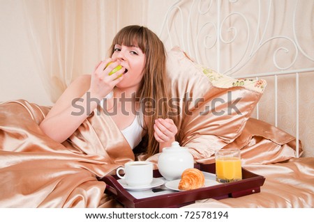 Woman eating breakfast and drinking coffee in bed. Young woman smiling looking at camera