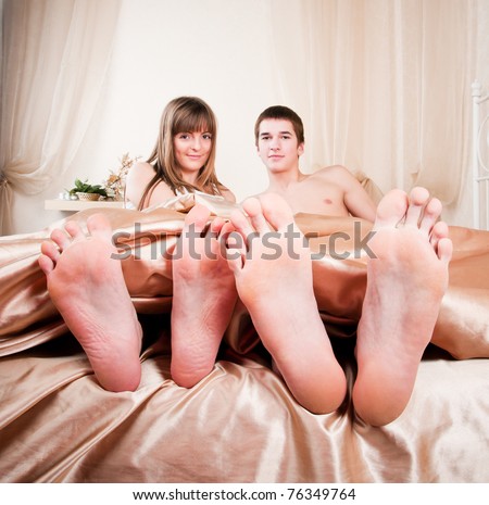 The bared heels of pair in stick out from under bed-sheets