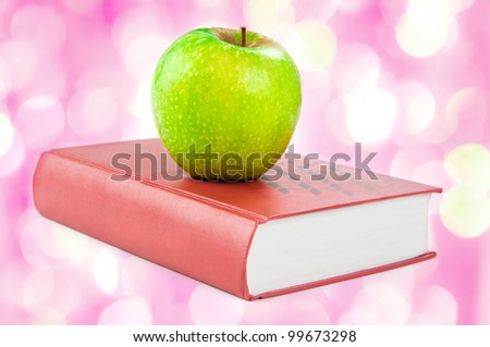 A green apple on a book   with pink lights in the background