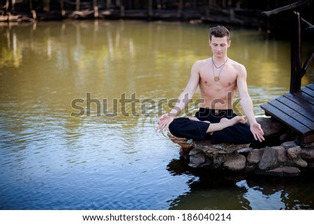 Outdoor yoga session in beautiful garden with a lake - young man meditating