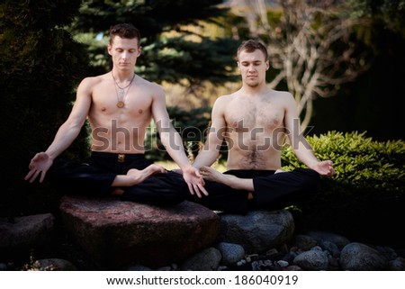Outdoor yoga session in beautiful garden - two young man meditating