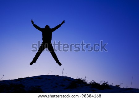 A blue-tonality photo of a happy, successful man on a hill who is jumping with hands up. Made during sunset in Kracow, Poland.