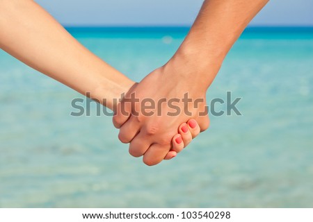 Hands of two people close up. They are standing near the sea and holding each other