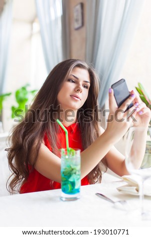 A smiling woman in restaurant is talking photos on mobile phone