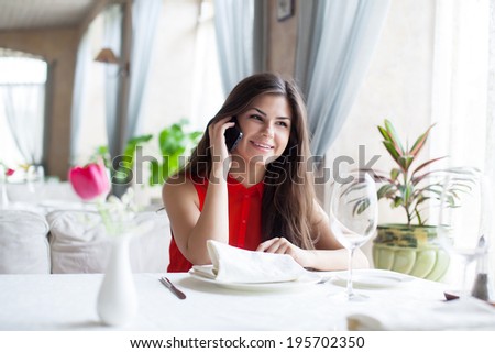 A smiling woman in restaurant is talking to mobile phone