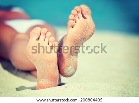 Woman\'s feet on the white sand near the sea, vintage-style photo.