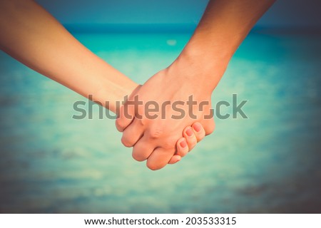 Hands of two people close up. They are standing near the sea and holding each other