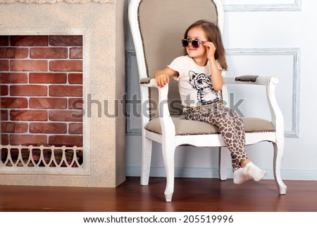 Little girl is sitting on the chair near fireplace