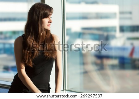 Young brunette woman is looking through the window on the planes and waiting to departure in the airport
