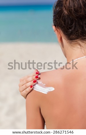 A woman is applying sunblock on her back. Close-up